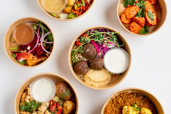 Selection of The Conscious Farm Kitchen prepared meals in compostable containers (falafel bowl, roasted carrots with harissa, souvlaki bowl, cauliflower and lentil curry, and blood orange salad)