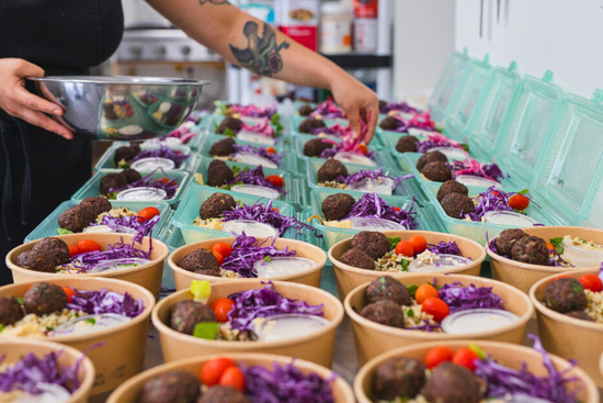 Meal prep in The Conscious Farm Kitchen. Celeste is adding pickled red onions to our falafel bowls.