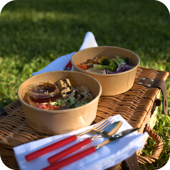 Two of The Conscious Farm Kitchen prepared meals on top of a picnic box with cutlery.