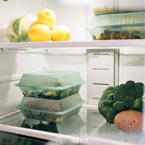 Inside of a fridge with The Conscious Farm Kitchen meals in reusable containers stacked on top of each other.